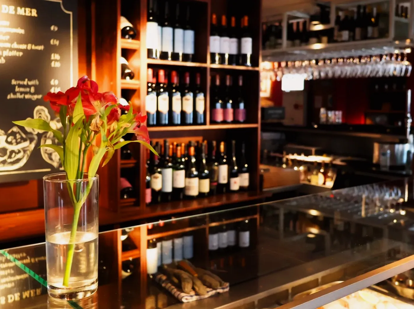 The bar at Chez Bernard with red flowers and bottles behind