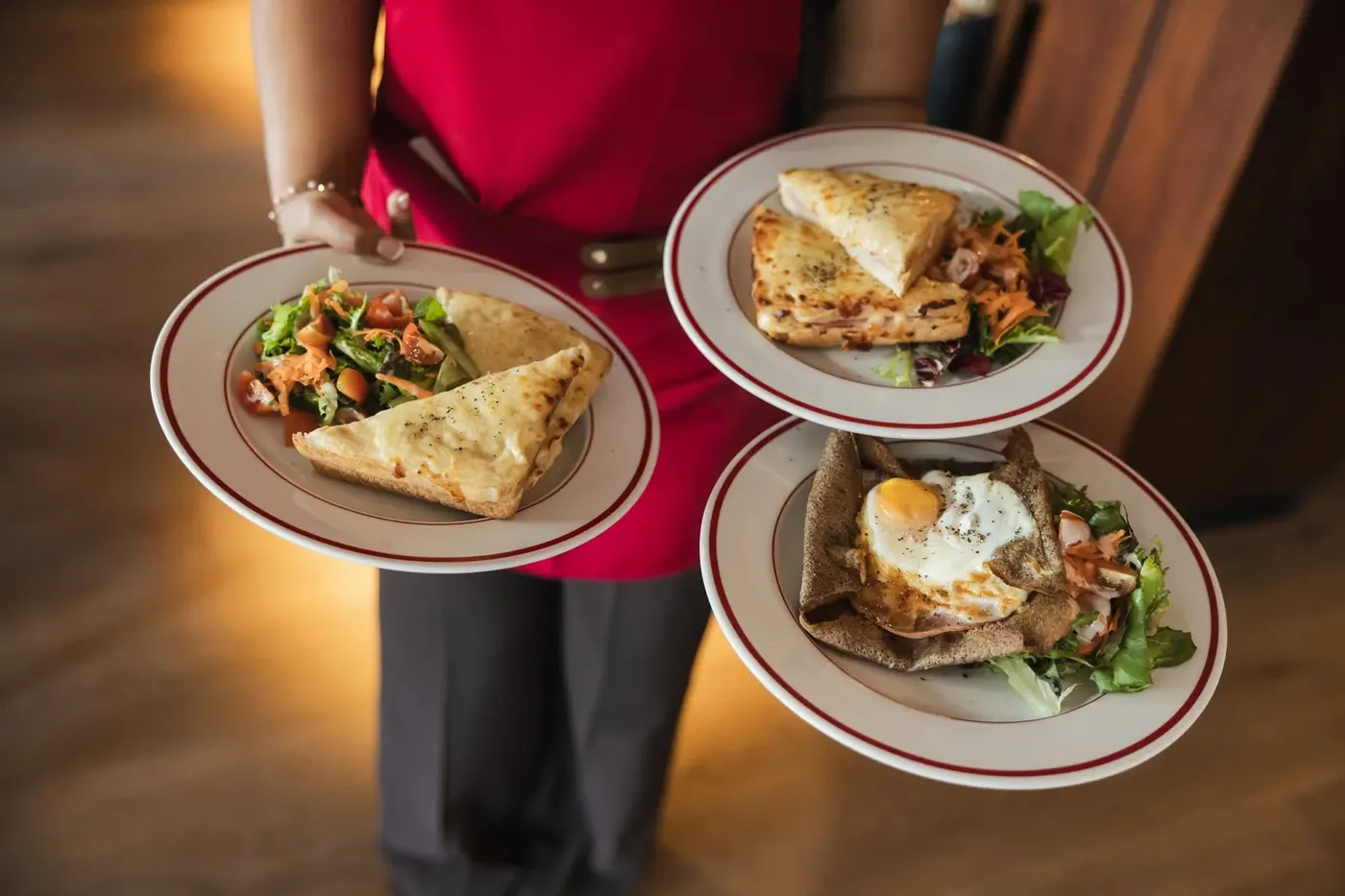Three plates of galettes and tartines with dressed salad, carried to a table