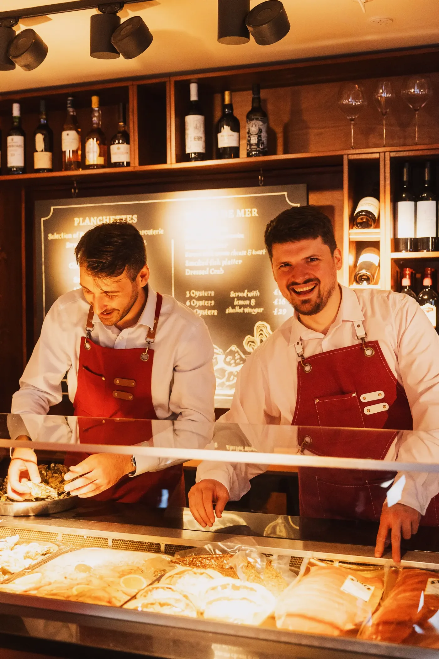 Two members of the Chez Bernard team behind the deli counter in red aprons